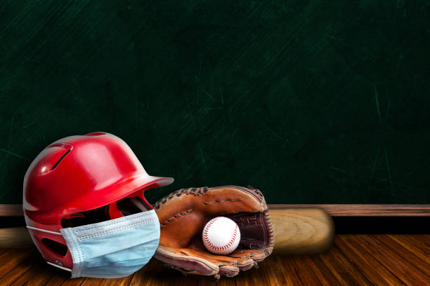 Baseball Helmet Wearing Mask With Chalkboard Background and Copy Space Baseball helmet wearing surgical mask on a background chalk board with copy space for text. Concept of COVID-19 coronavirus pandemic affecting baseball season due to game or league suspensions or cancellations. face guard sport photos stock pictures, royalty-free photos & images