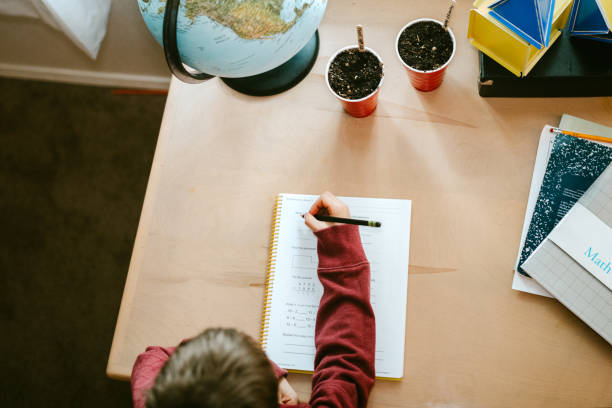 homework time images Boy Focuses on Lessons at Homeschool A boy works on his math lesson while doing school at home. Normal education, or a the new normal for social distancing during Covid-19 lockdown. homework table stock pictures, royalty-free photos & images