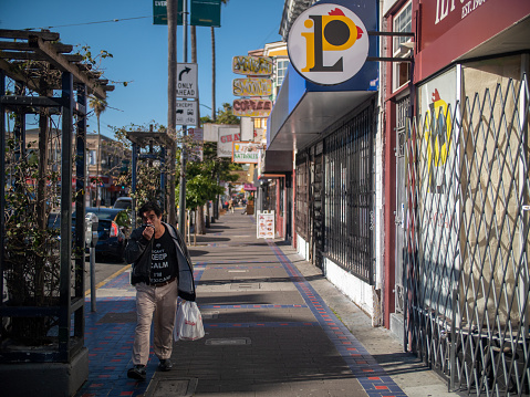A Mexican man covering his mouth is walking down the nearly empty street in the Mission District of San Francisco. April 2nd, 2020.