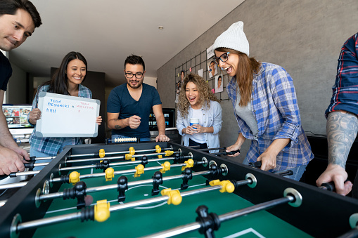 Excited group of Latin American workers having fun playing foosball at the office