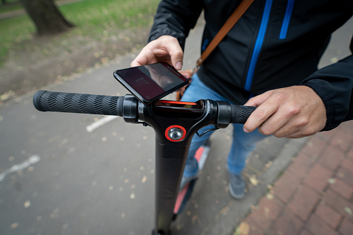 Close-up on a man renting an electric push scooter with his cell phone using a mobile app â technology concepts