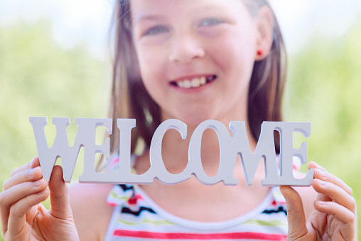Little laughing girl holding the words WELCOME in her hands - shallow depth of field - focus on lettering