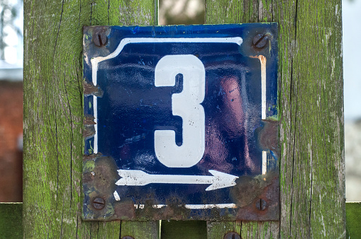 Weathered grunge square metal enameled plate of number of street address with number 3 closeup