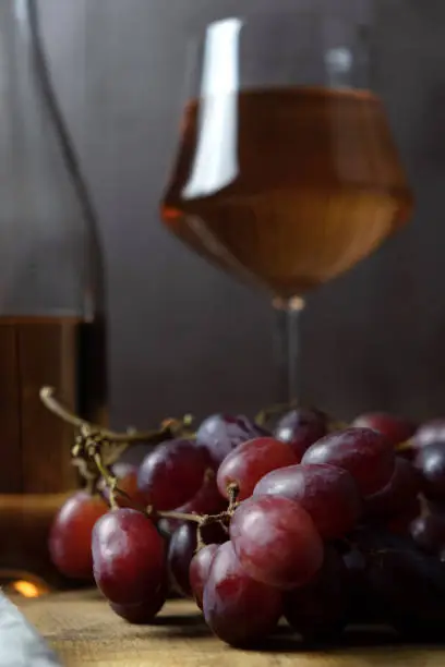 Photo of A close-up of a bunch of grapes, and in the background a bottle and a glass of pink wine are out of focus. vertical orientation