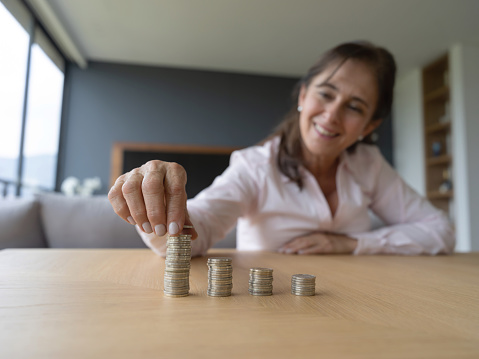 Happy senior woman at home stacking coins on table smiling - Home finance concepts