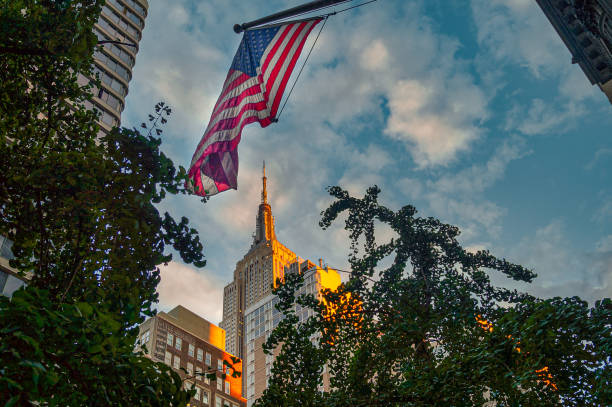 low perspective view to the illuminated empire state building in new york and the hanging usa star spangled banner flag. - star spangled banner imagens e fotografias de stock