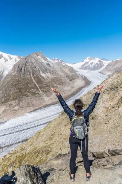 View from behind of a woman with her arms raised looking at Aletsch Glacier from Eggishorn viewpoint, Bernese Alps, canton Valais, Switzerland, Europe