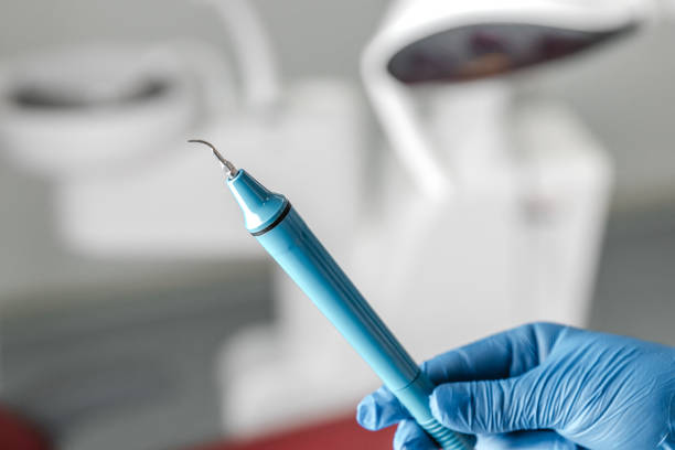 самка руки стоматолога в синих перчатках держит ультразвуковую машину для чистки зубов, удаляя исчисление и налет. гигиена полости рта и ко - machine teeth стоковые фото и изображения