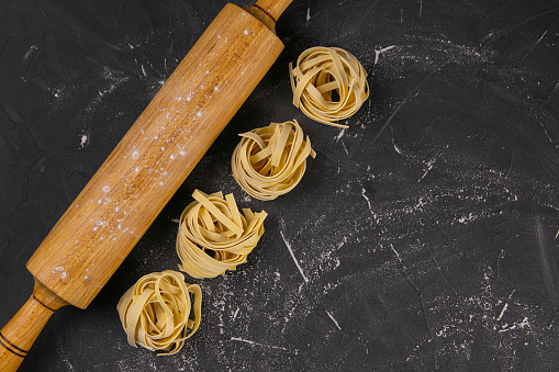 Raw tagliatelle with rolling pin for dough on black background. Top views with clear space