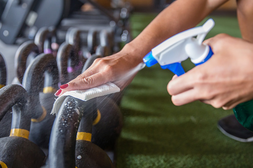 Close up shot female athlete spraying kettlebells with disinfectant ,and wiping the handle before workout ,precautions of Coronavirus