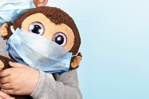 Little middle-eastern preschool kid boy plays with his toy monkey in medical face mask during novel coronavirus pandemic. COVID-19 outbreak. Boy at quarantine