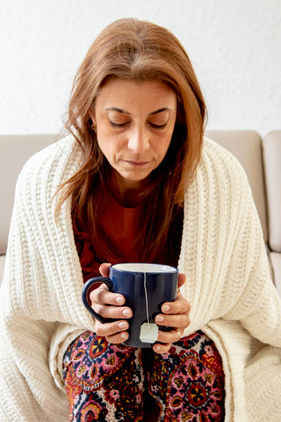 istock Sick woman on couch drinking tea 1216690483