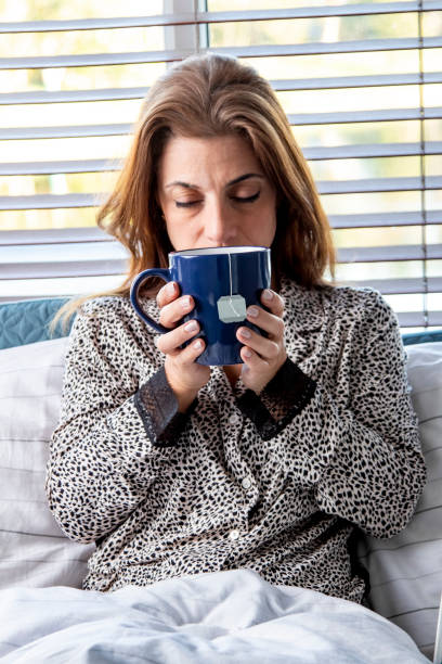 istock Sick woman in bed drinking hot tea 1216690552