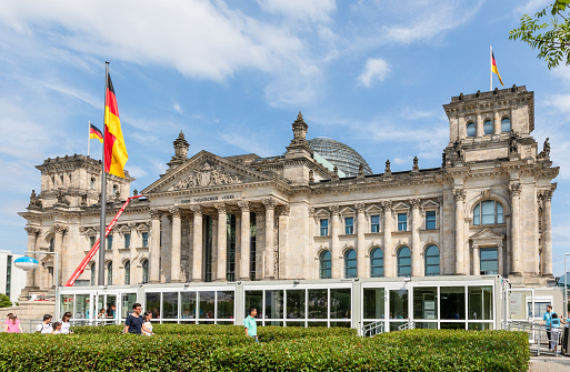 Berlin, Germany - August 10, 2017: Reichstag building or Reichstagsgebäude in Berlin, with German Unity Flags waving. Symbol, heritage and tourist attraction.