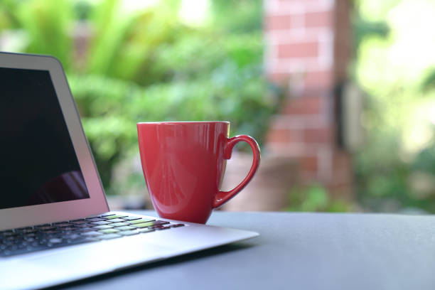 istock Computer laptop with coffee in red cup. Garden background. 1216696610