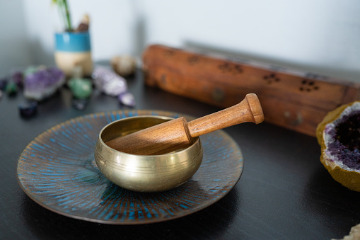 This is a photograph of a small Tibetan sound bowl with a wooden mallet indoors with crystals and an incense holder at home.