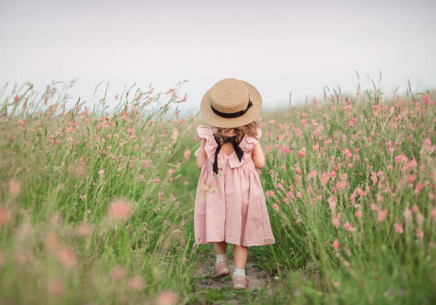 아름다운 드레스를 입은 어린 소녀는 여름 날에 꽃밭에 간다. - flower hat fun child 뉴스 사진 이미지