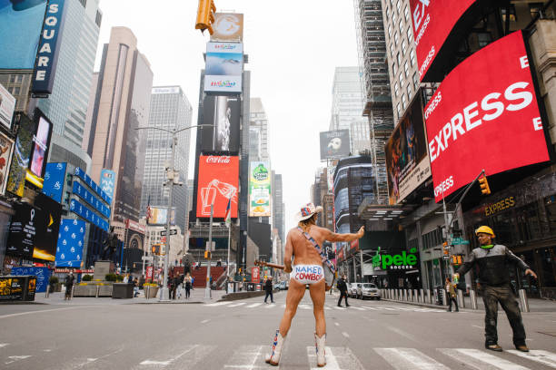 A large group of pedestrians crossing 7th Avenue in Times Square in Manhattan, New York City. Yellow taxi cabs, a large illuminated USA flag and colorful advertising billboards are visible in the background, horizontal orientation, USA.