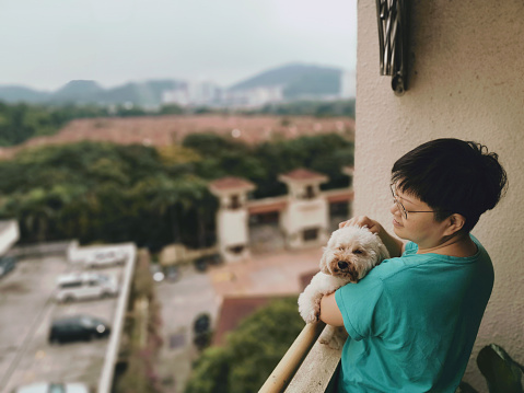 an asian chinese woman carrying her pet toy poodle looking from her balcony during the restriction movement order lockdown