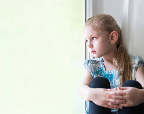 istock Sad child girl by the window 1216742879
