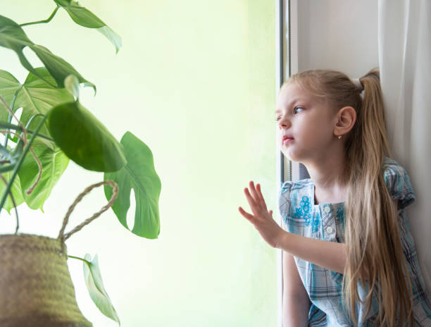 istock Sad child girl by the window 1216743238