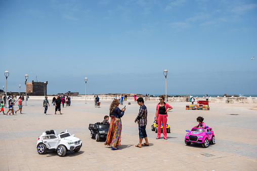Essaouira, Morocco - June 09, 2015: Mothers talk near the beach, while their kids play with electric cars.
