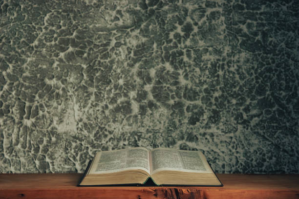 istock Open bible on a brown old wooden table. Beautiful gray white wall background. 1216744532