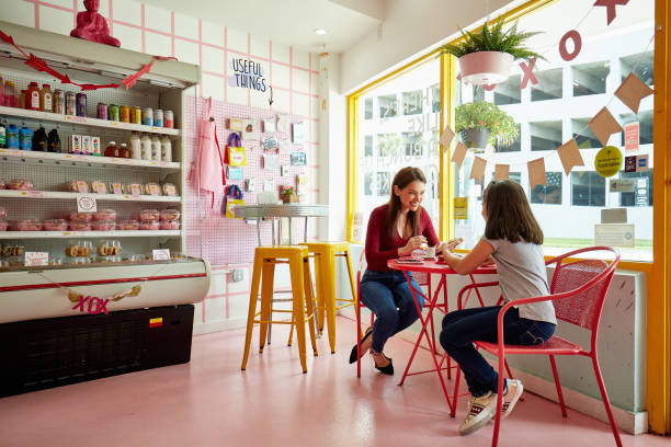 Mid adult Hispanic mother and preteen daughter enjoying doughnuts and beverage at cafe table in gourmet bakery.