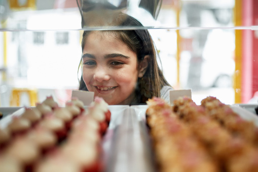 Personal perspective of smiling 9 year old girl admiring gourmet cupcakes in display case of Miami vegan bakery.