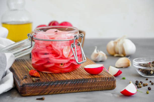 nourriture fermentée. radis mariné avec l’oignon, l’ail et les épices dans un bocal sur une planche à découper sur un fond en béton foncé. orientation horizontale. copier l’espace. - radis photos et images de collection