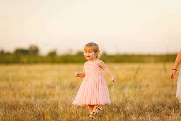 baby girl chasing soap bubbles on the sloping wheat field at sunset in village