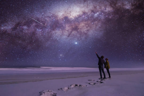 The couple and the star Couple holding hands looking and pointing in amazement at a shooting star while standing on a secluded beach. milky way photos stock pictures, royalty-free photos & images