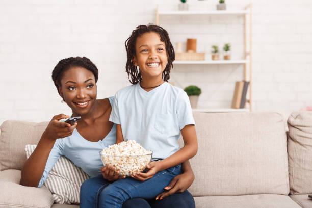 Black family eating popcorn and watching tv together Family Time Concept. Happy african mom and child sitting on sofa, eating popcorn and watching tv, empty space popcorn snack bowl isolated stock pictures, royalty-free photos & images