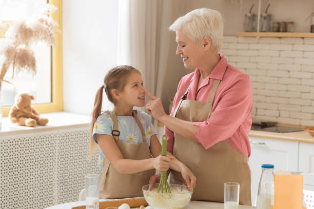 istock Time for cooking. Grandmother with her granddaughter having fun while baking in sunlit kitchen, blank space 1216749579