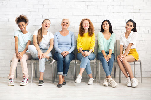 Female Togetherness. Smiling Ladies Of Different Age And Ethnicities Sitting On Chairs Indoor.