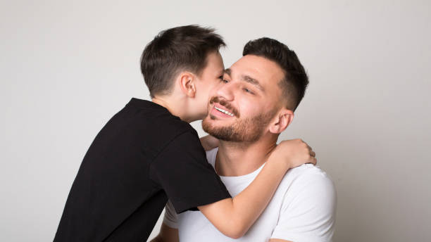 istock Cheerful boy hugging with his father, gray studio background 1216749989