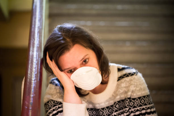 istock Sad woman wearing protective face mask sitting on stairs 1216750041