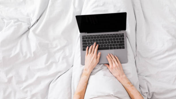 istock Woman working in bed and typing on laptop with blank screen 1216751397