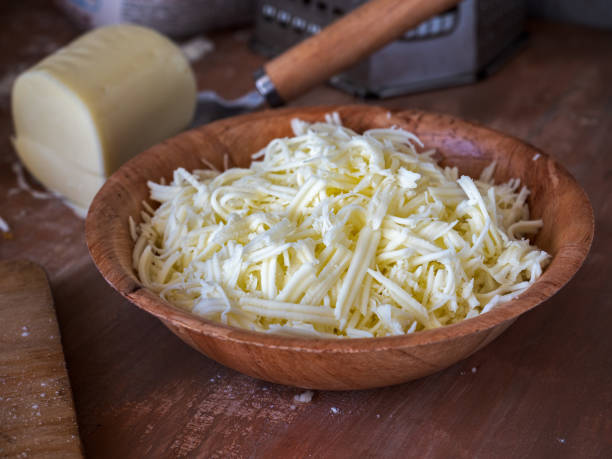 Grated cheese for making pizza in a deep bamboo plate by a large clan on table Grated cheese for making pizza in a deep bamboo plate by a large clan on a wooden table shredded mozzarella stock pictures, royalty-free photos & images