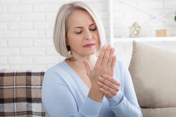 middle aged woman suffering from pain in hands. woman massaging her arthritic hand and wrist - osteoarthritis doctor medicine healthcare and medicine imagens e fotografias de stock