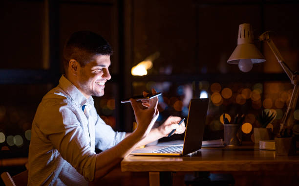 istock Smiling Businessman Using Voice Assistant In Modern Office At Night 1216755548