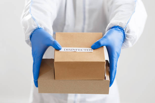 istock Man in protective suit and gloves gives disinfected boxes 1216755560