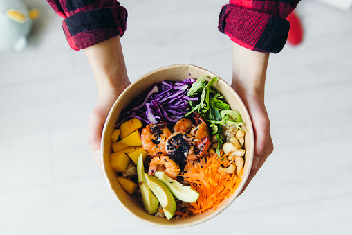 Woman holding healthy seafood Japanese Hawaiian poke bowl with mango and avocado - eating at home during quarantine, Asian cuisine delivery