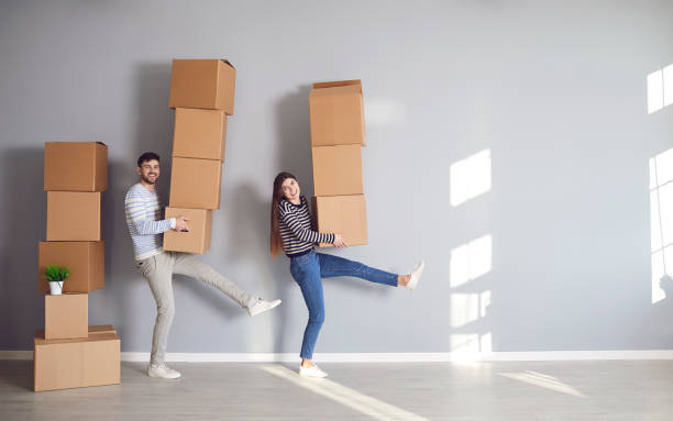 le couple drôle heureux retient des boîtes en carton pour se déplacer dans la nouvelle chambre de maison d’appartement - apartment contemporary action packing photos et images de collection