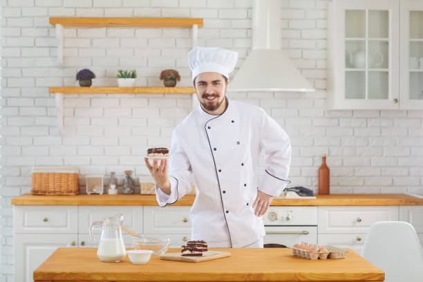 istock Confectioner man smiles while standing with cake in his hands at the kitchen bakery 1216756661