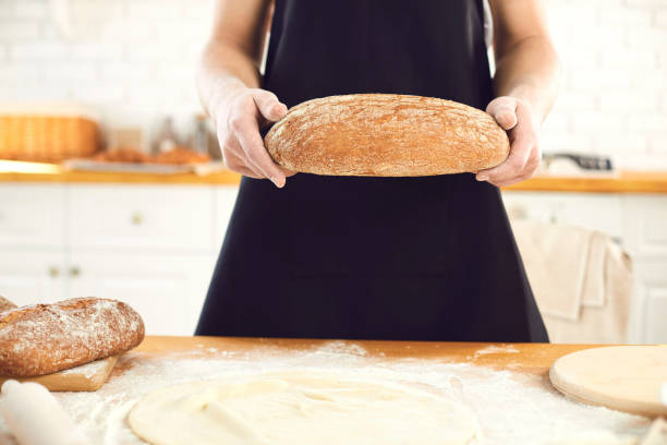 istock Baker man bearded man holds in his hands fresh bread standing in the kitchen. 1216756687