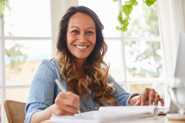 istock Smiling mature woman writing in a notebook while working at home 1216762479
