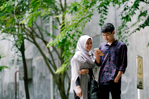Young Beautiful Muslim Couple Looking at Mobile Phone Together while Walking Ramadan Shopping malay couple stock pictures, royalty-free photos & images
