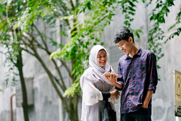 Young Beautiful Muslim Couple Looking at Mobile Phone Together while Walking Ramadan Shopping malay couple stock pictures, royalty-free photos & images