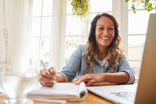 istock Mature woman writing notes and laughing while working from home 1216763922